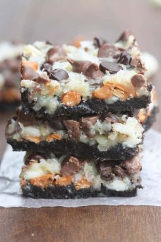A front view of a stack of three Oreo magic bars with an oreo crust and coconut chocolate chip topping.