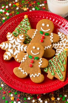 Gingerbread cookies on a red plate cut into gingerbread men shapes, trees and snowflakes. Decorated with royal icing and christmas sprinkles.