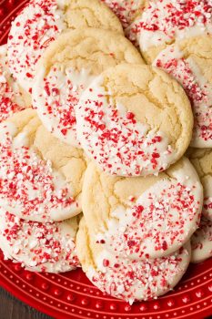 Sugar cookies flavored with peppermint, dipped in white chocolate and covered with crushed candy canes. Cookies are shown served on a red plate.
