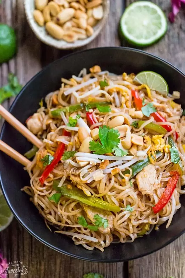 Easy and Authentic Chicken Pad Thai recipe in a large black serving bowl with brown chopsticks on a wooden table. 